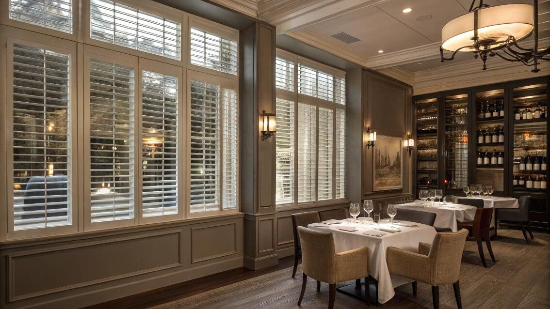 Upscale restaurant with tall windows featuring elegant white plantation shutters.