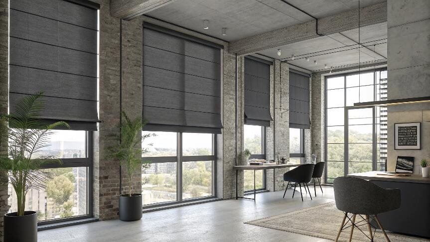 Modern loft office featuring large windows with dark Roman blinds.