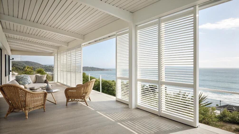 Coastal patio with white louvered shutters overlooking the ocean and hills.