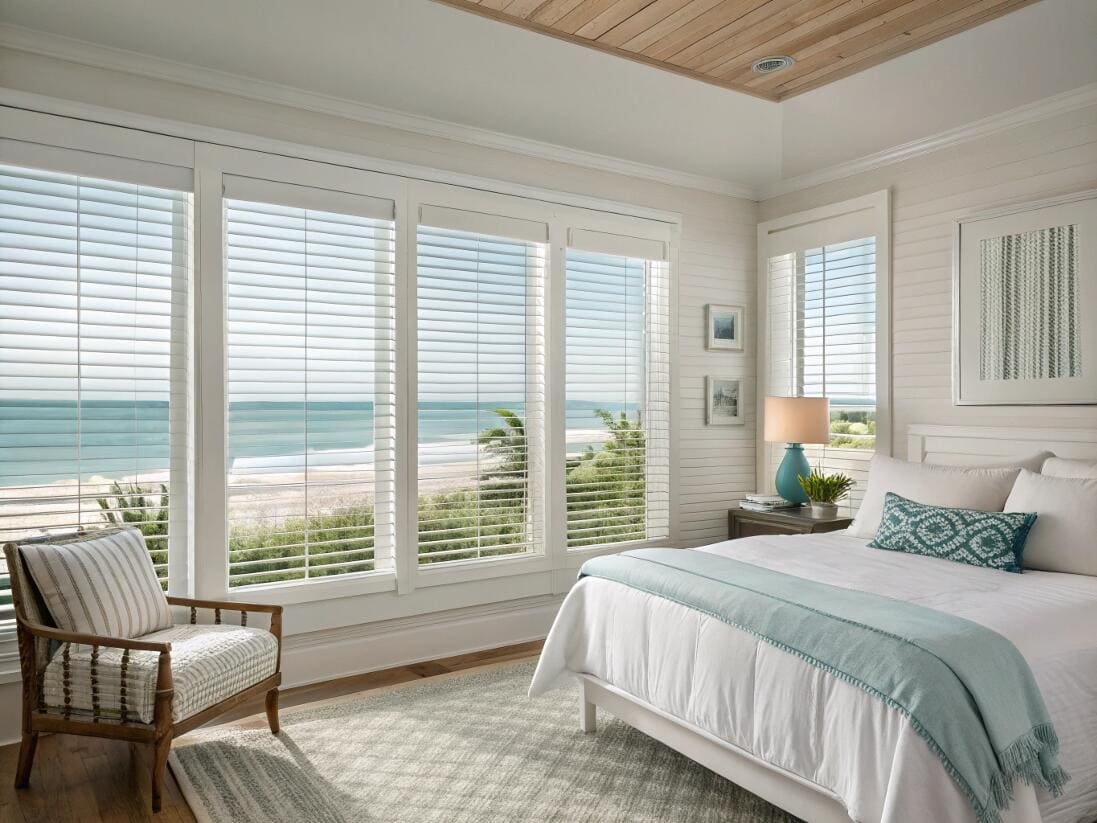 Coastal bedroom with crisp white faux wood blinds to enhance the beachside view.