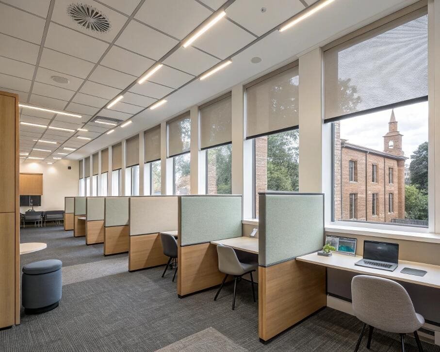 Commercial office space with numerous desks and dark gray roller shades.