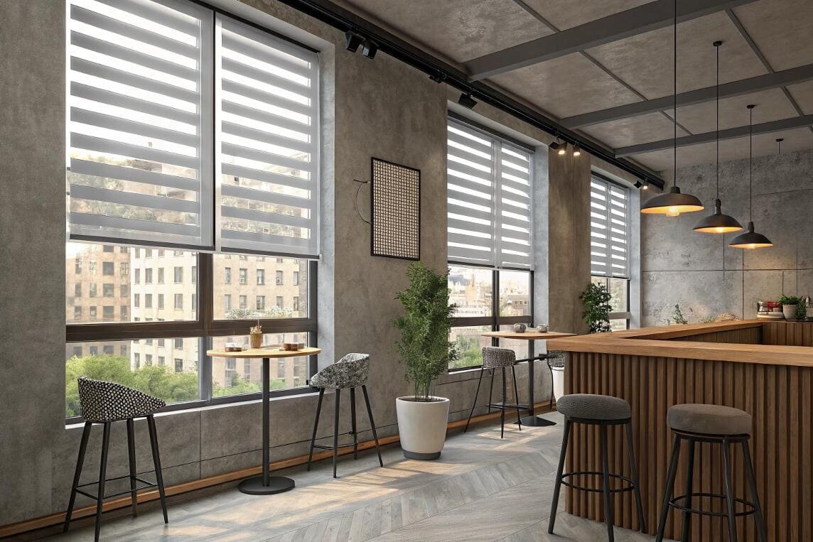 Trendy cafe interior with high tables and cityscape views framed by striped zebra blinds.
