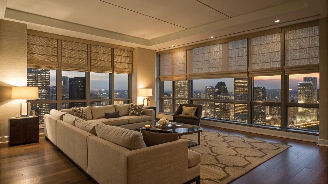 High-rise living room with cityscape and neutral fabric Roman shades.