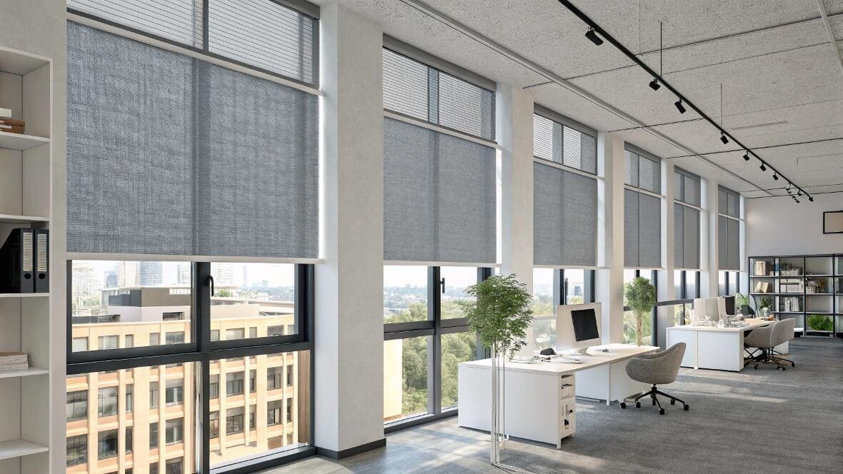 Spacious modern office with tall windows and grey roller shades for glare control.