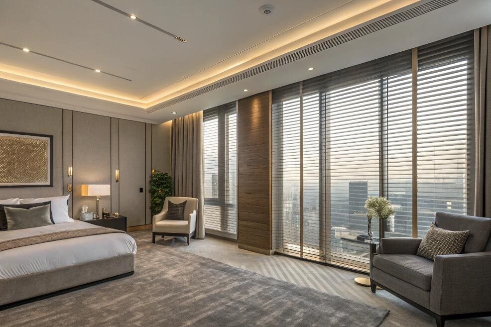 Motorized wood blinds provide effortless light control for floor-to-ceiling windows in a luxury bedroom.